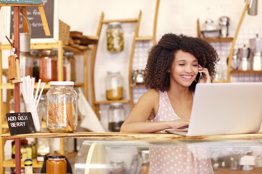 Small business owner in their store, on the phone and looking at a laptop screen.