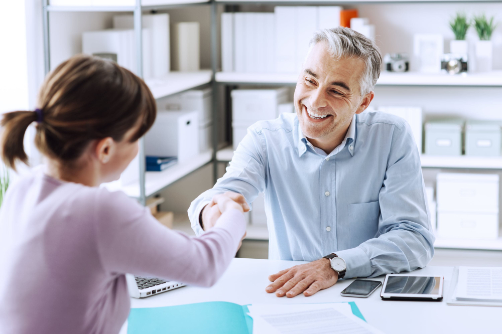 Recruitment agent smiling and shaking hand of successful female applicant.