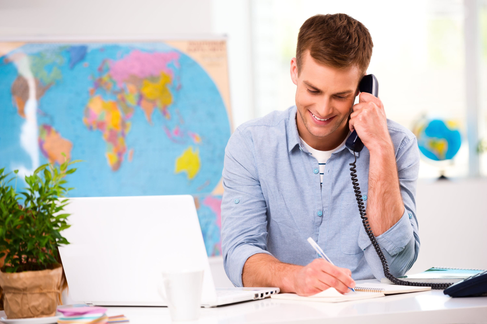 Smiling travel agent on phone with world map in background.