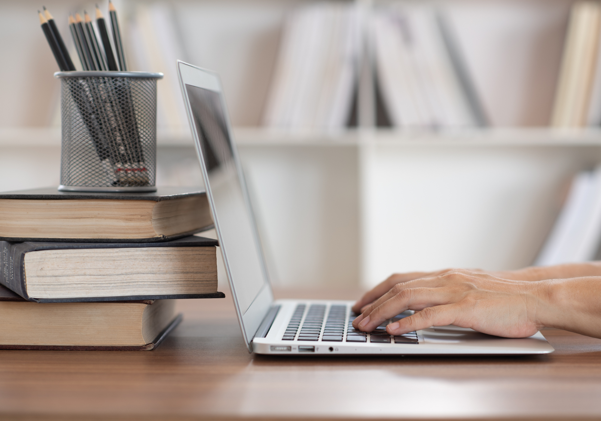 Person typing on laptop with books stacked next to the laptop.